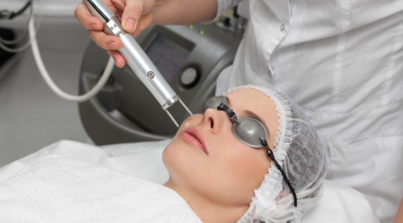 Woman lying on a table with protect glasses on eyes getting a laser skin treatment in healthy beauty spa salon