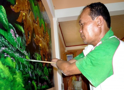 Thầy Khanh Rông họa thêm chi tiết cho bức tranh sơn dầu mừng nhà mới. (Ảnh: Báo Cà Mau)