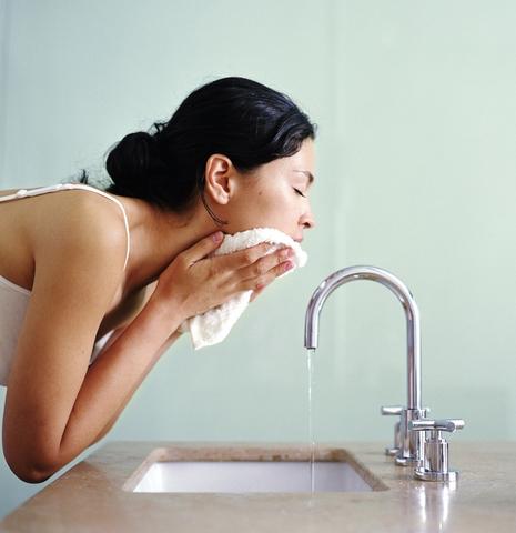 Woman washing face with wash cloth over sink, side view