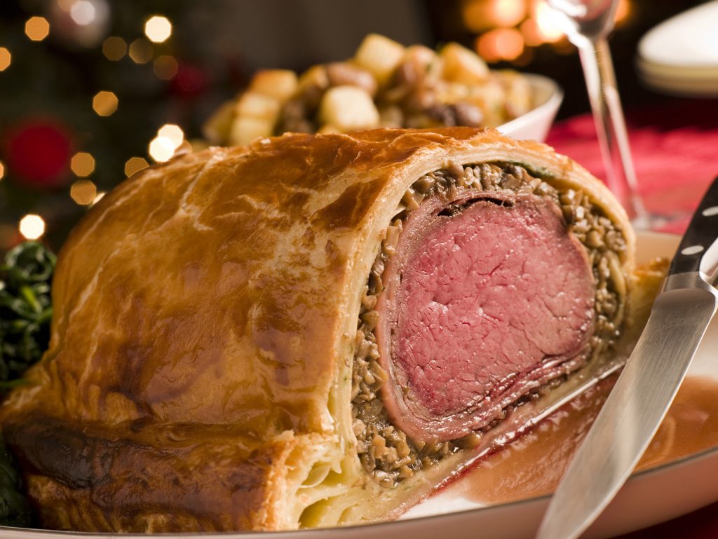 Carved Beef Wellington On Dining Table With Christmas Tree In Background