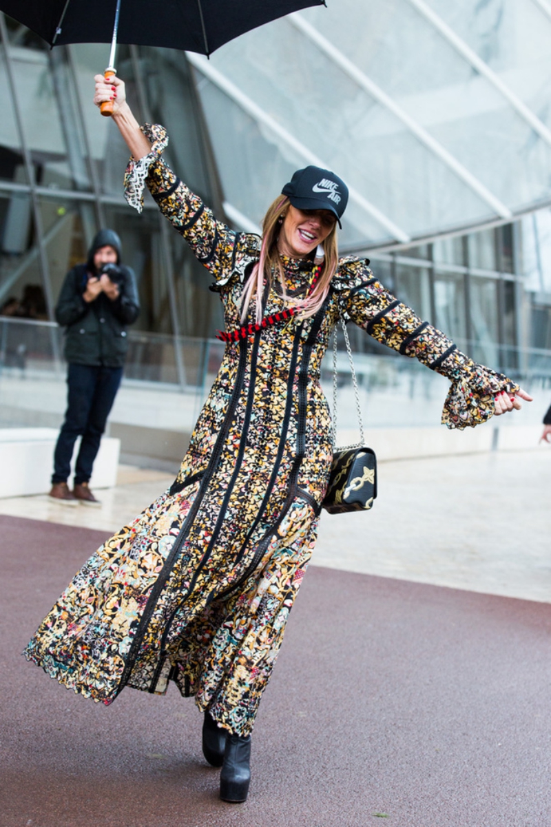 "Nữ hoàng làm quá" Anna Dello Russo bất chấp cơn mưa ở Paris vẫn diện bộ đầm nổi bật của Louis Vuitton cùng túi xách Twist cùng thương hiệu. Phụ kiện để đối mặt với trời mưa của bà là mũ thể thao Nike và chiếc dù màu đen. 