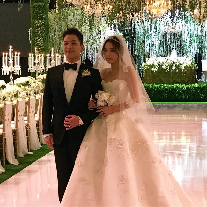 Chú rể Taeyang lịch lãm trong tuxedo đen với sơ mi trắng và nơ bướm không giấu được niềm hạnh phúc khi đứng bên cô dâu Min Hyo Rin xinh đẹp mặc váy cưới Oscar de la Renta.