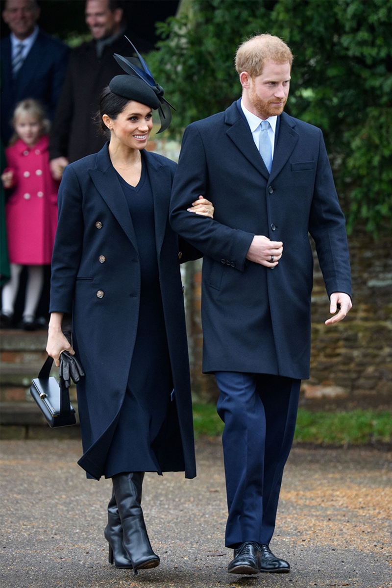 Công nương Meghan Markle mặc thiết kế đầm dài ngang bắp chân màu xanh navy của Victoria Beckham phối cùng áo khoác dài, boots da cao cổ và chiếc túi xách vô cùng đặc sắc. Tất cả đều đến từ thương hiệu Victoria Beckham. 